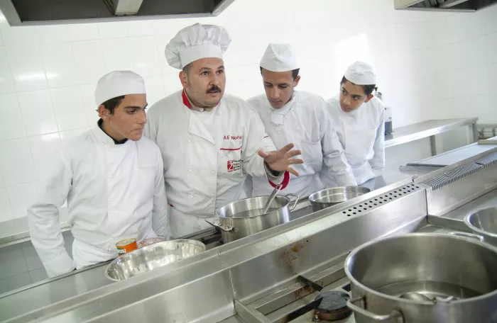 one cook teaching 3 men in a professional kitchen