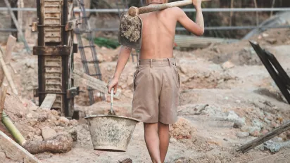 A child carrying a bucket and a shovel on a construction site.