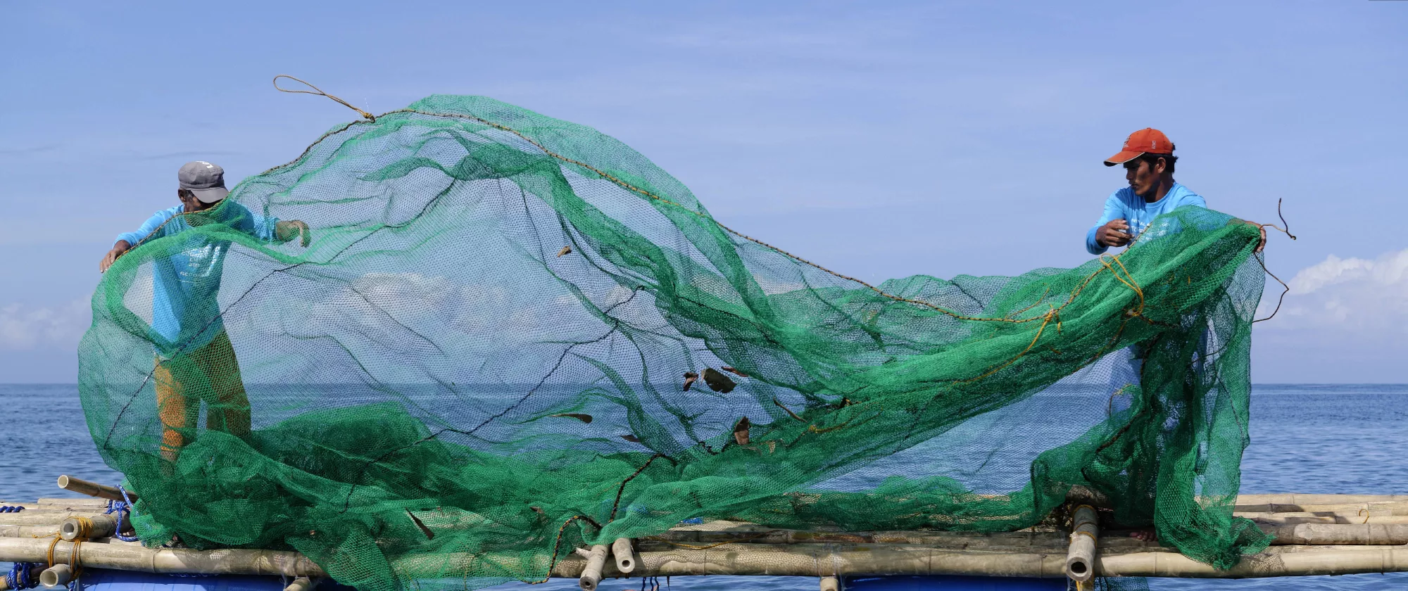 Fishers folding a green fishing net next on a handmade boat